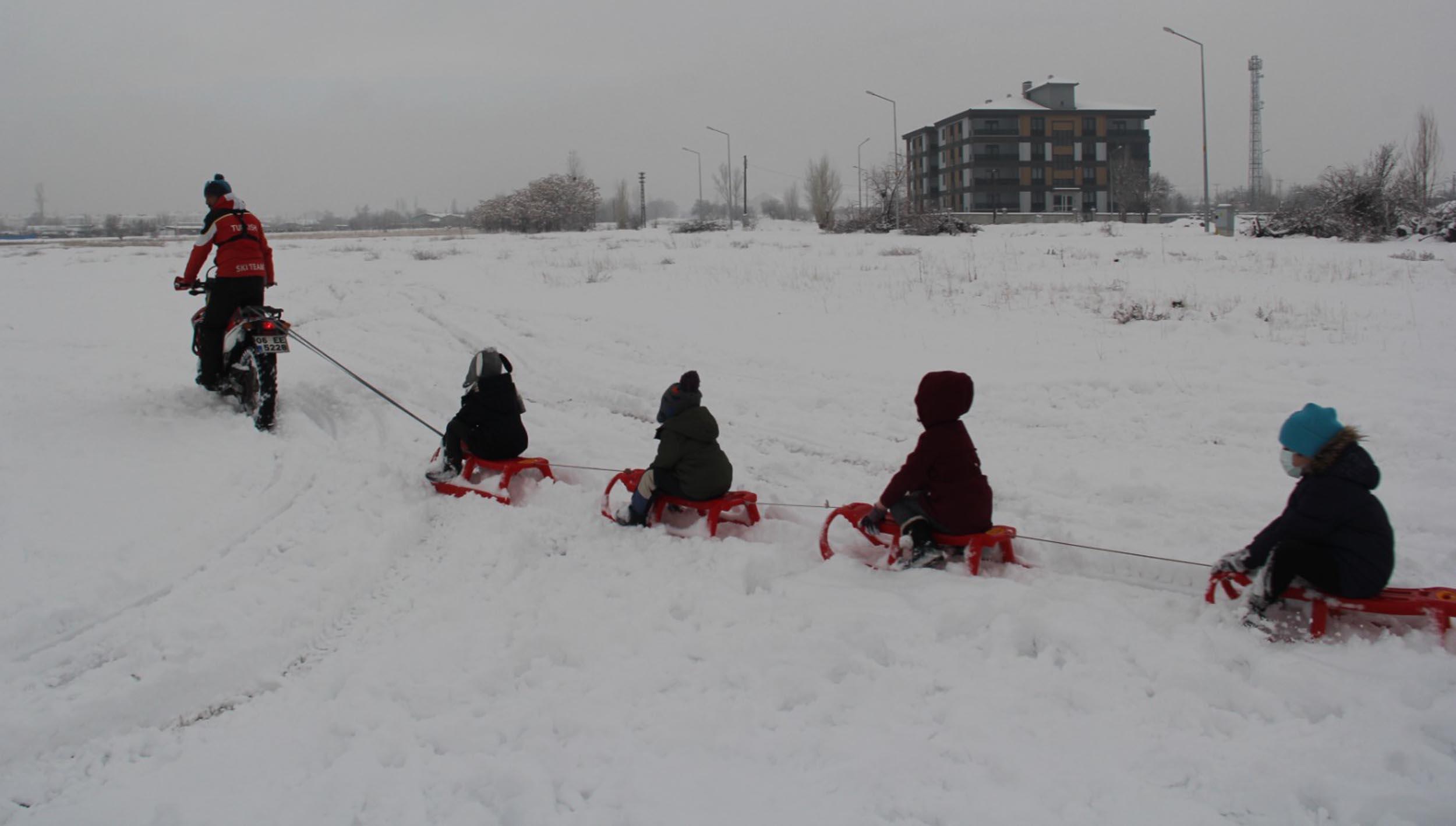 Motosiklete bağladığı kızaklarla çocukları karda eğlendirdi