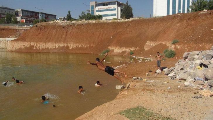 Çocuklar, inşaat temelini dolduran kirli suda yüzüyor