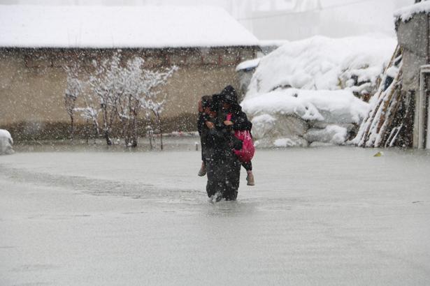 Evinin önünde biriken su nedeniyle çocuklarını sırtında taşıyor