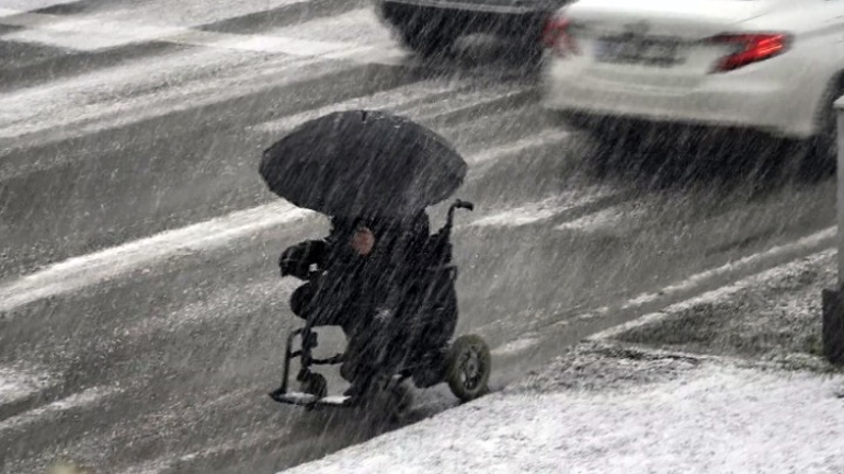 Tekerlekli sandalyesinde elindeki şemsiye ile karda ilerledi